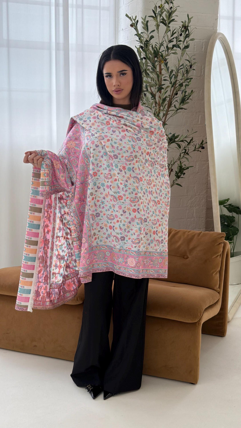 Woman holding a white and pink floral patterned shawl in a room with a couch and plants.