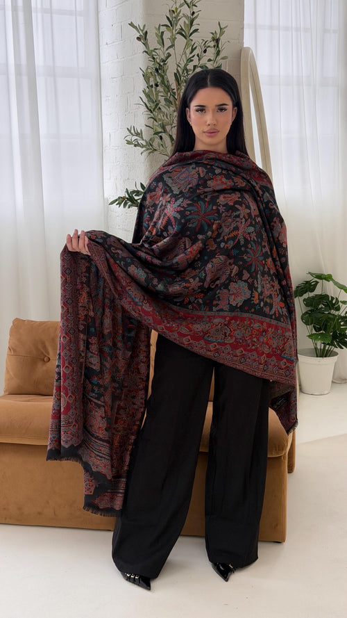 Woman holding a black patterned pashmina shawl scarf in a living room setting