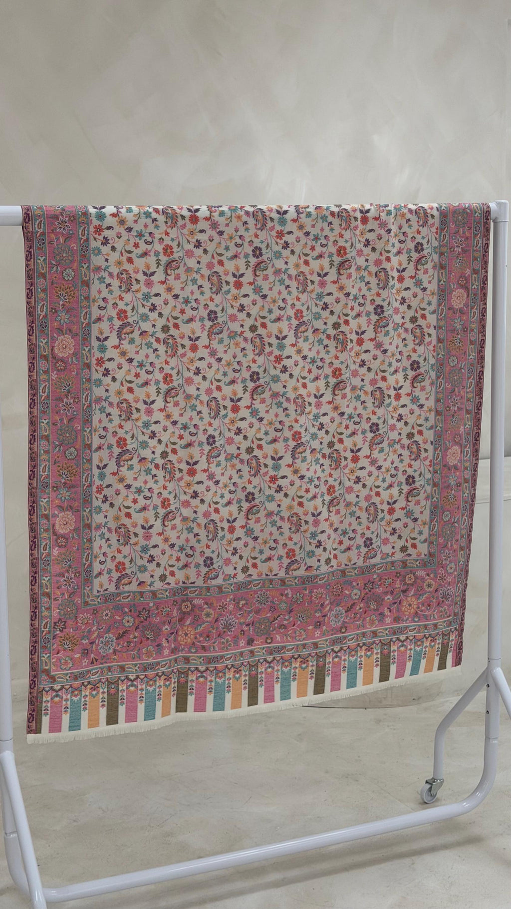 white and pink floral patterned shawl on a white rack against a light background