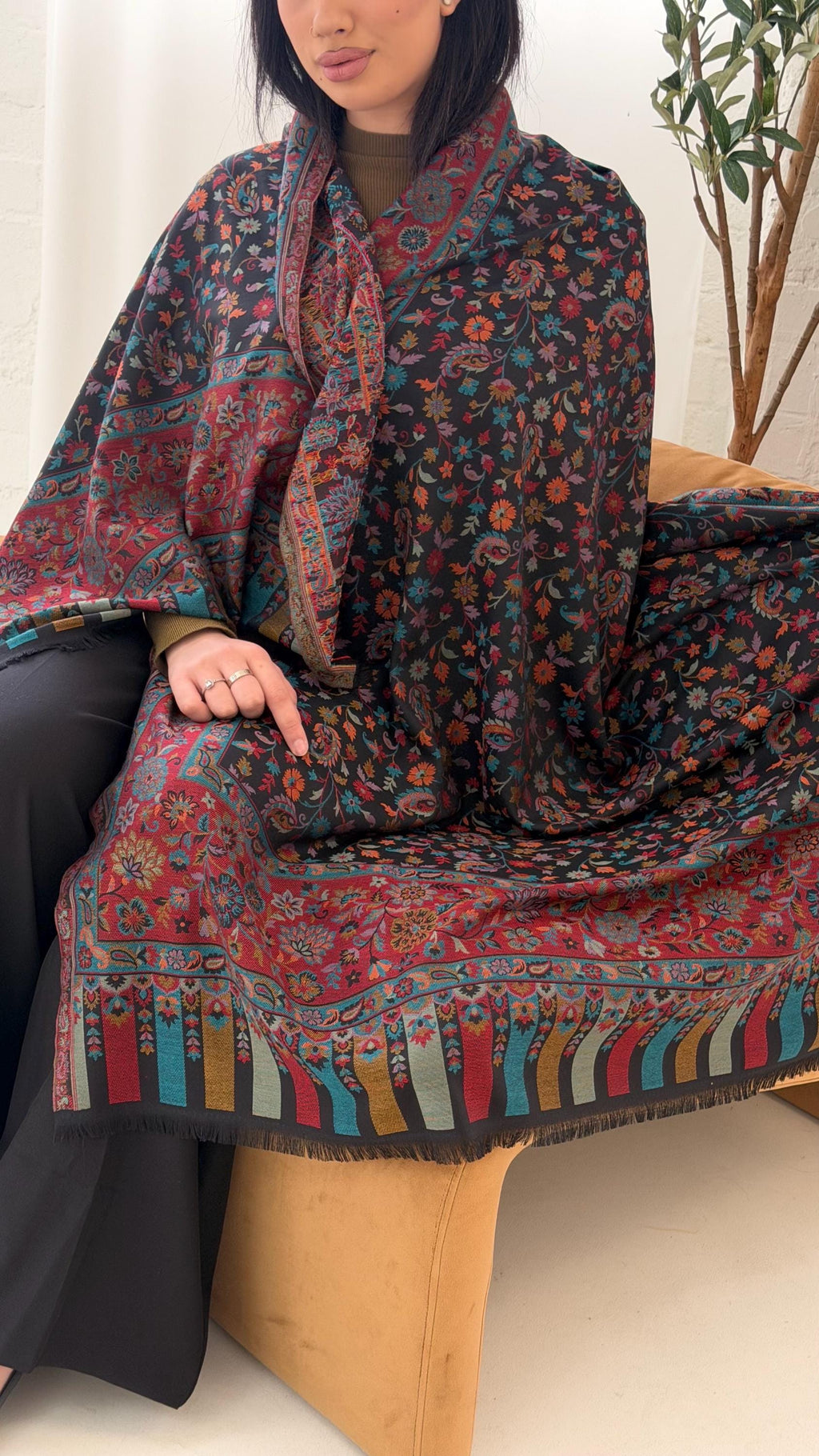 Person wearing a colorful patterned scarf sitting on a wooden stool.